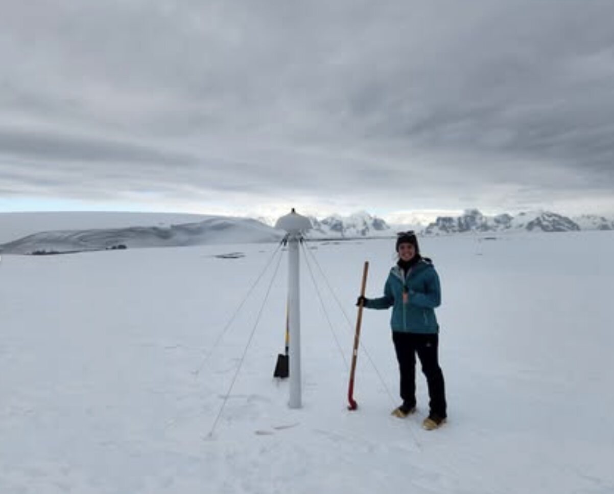 Jacquelyn Veatch standing with a shovel beside a radar installation in the Antarctic snow